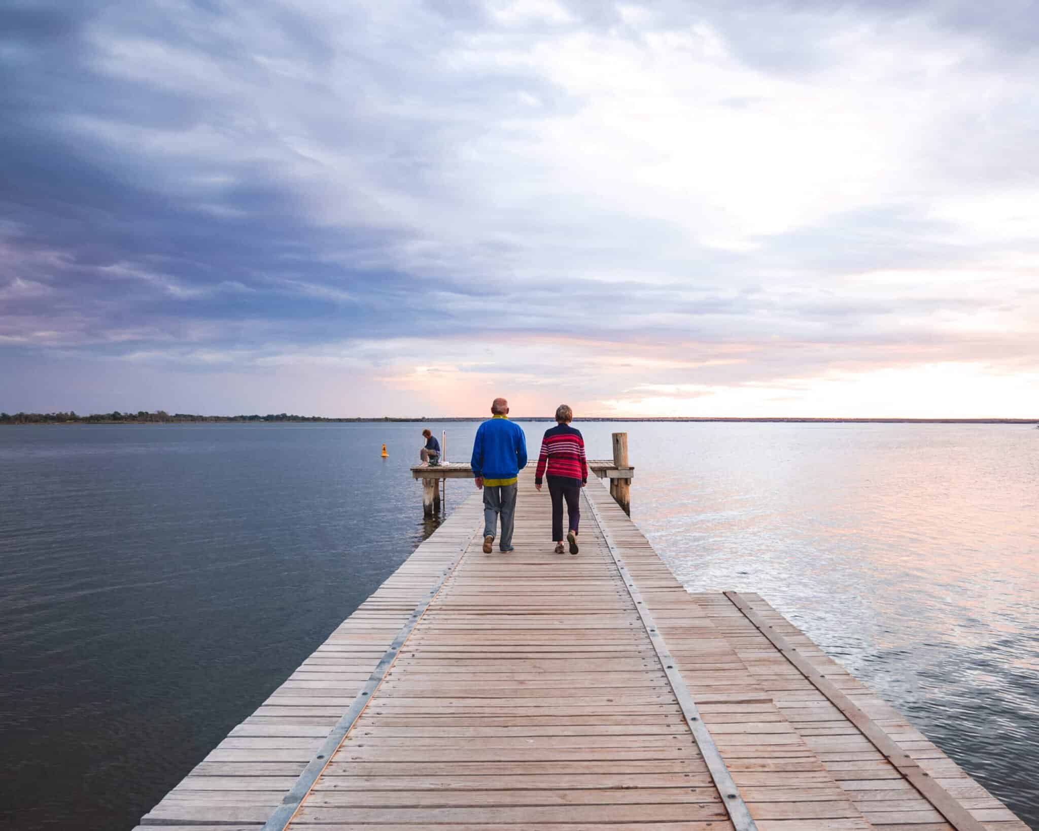 Two people walking to end of jetty on lake at sunset
