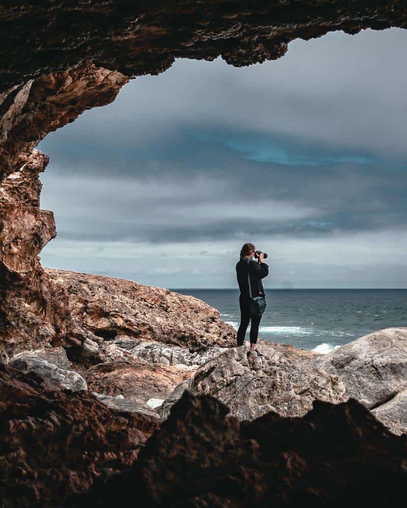 Rock overhangs at Cape Carnot- view from cave showing woman taking photo with ocean in the background