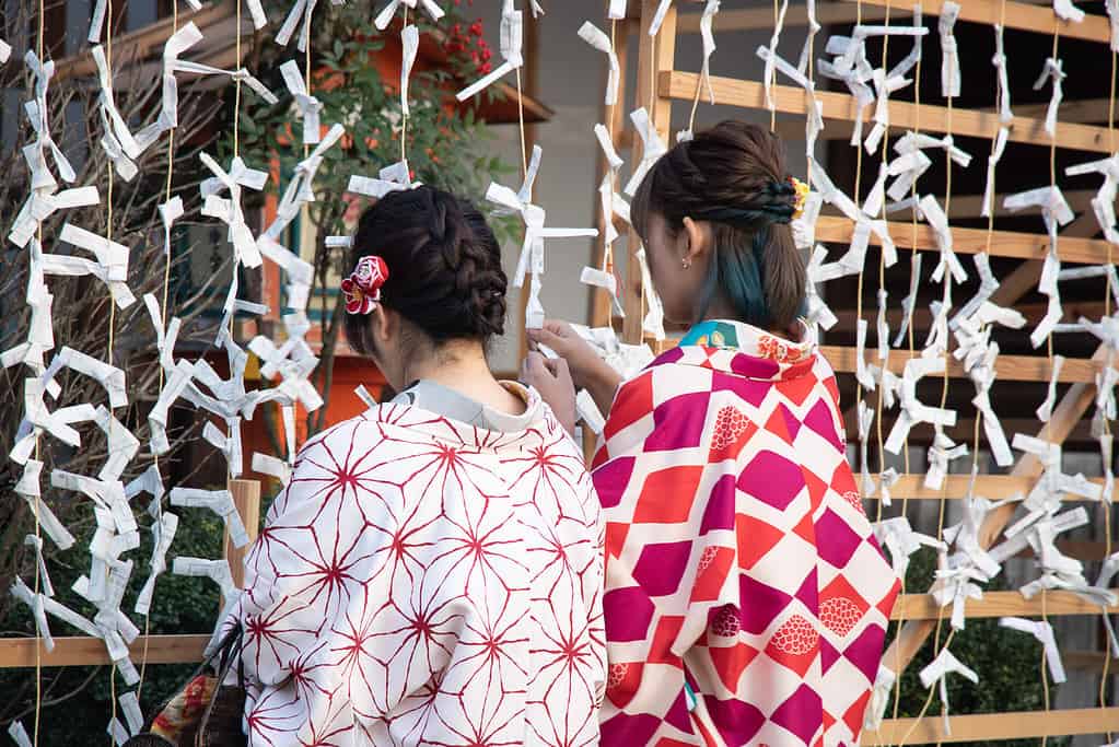 Two Japanese women at temple with string of paper prayers